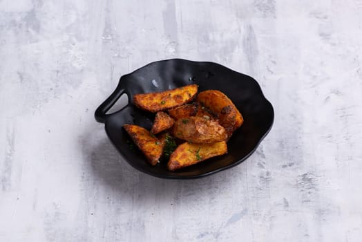 A closeup shot of tasty Potato wedges on a black dish on a white marble surface