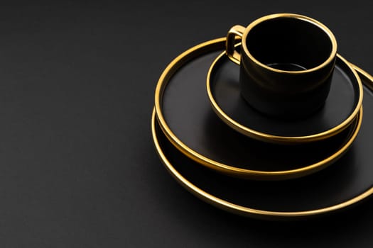 A set of black and golden ceramic plates and cup on a black background