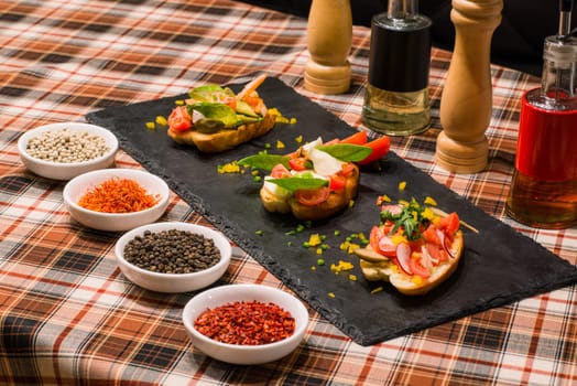 A closeup of serving table with tasty sandwiches or bruschetta with vegetables and spices on black board