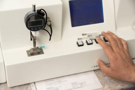 A closeup shot of a hand using a medical machine to test and manufacture pharmaceutical syringes