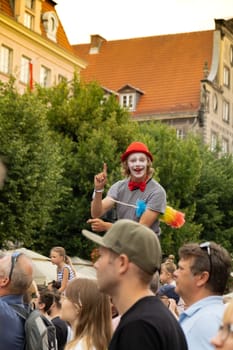 Gdansk, Poland - 9 August 2022 Portrait of cool clown in bright wig. Parade during Dominic's Fair in Gdansk. Entertainment festival in street stilts walker man in red juggling smiling. Theatrical performance for children at the