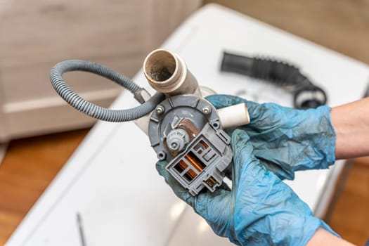 a broken old washing machine water pump in the hands of a home appliance repairman. Repair of a used washing machine. A jammed pump. calcium-magnesium deposits. Scum.