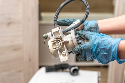 a broken old washing machine water pump in the hands of a home appliance repairman. Repair of a used washing machine. A jammed pump. calcium-magnesium deposits. Scum.