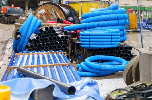 Blue and black pipelines of various diameters, concrete products and cables lie on a construction site on the street. Repair of communications.