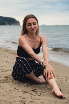 Young woman siting on blurred beachside background. Attractive female enjoying the sea shore. travel and active lifestyle concept. Springtime. Relaxation, youth, love, lifestyle solitude with nature. Wellness wellbeing mental health inner peace Slow life digital detox