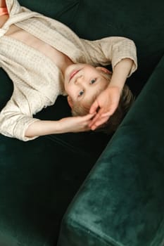 Portrait of a boy in a beige bathrobe, who lies on a green sofa and looks at the camera.