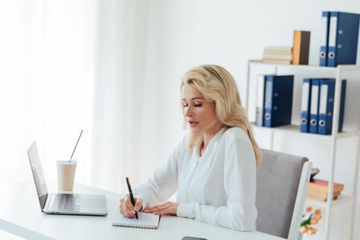 a woman in the office with a laptop computer records in a notebook remote work conversation on skype internet online communication