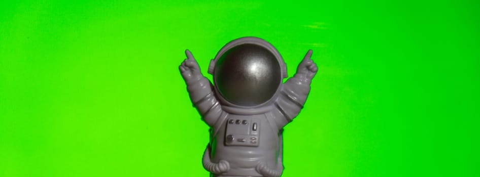 Plastic toy astronaut on green chroma key background Template Mock up Copy space. Concept of out of earth travel, private spaceman commercial flights. Space missions and Sustainability