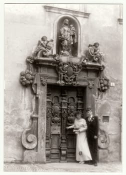 THE CZECHOSLOVAK SOCIALIST REPUBLIC - CIRCA 1980s: Vintage photo shows young newlyweds - bridal couple in front of historical door. Retro black and white photography.