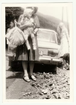 THE CZECHOSLOVAK SOCIALIST REPUBLIC - CIRCA 1980s: Vintage photo shows mother holds a small girl. They stand in front of car - brand LADA, car made in USSR. Retro black and white photography.