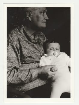 THE CZECHOSLOVAK SOCIALIST REPUBLIC - CIRCA 1970s: Vintage photo shows grandmother cradles todlder with dummy. Retro black and white photography. Circa 1970s.