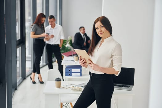 Woman holds tablet. Group of people in official formal clothes that is indoors in the office.