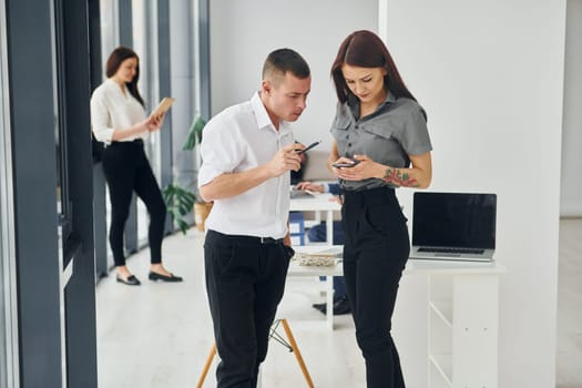 Man with woman using phone. Group of people in official formal clothes that is indoors in the office.