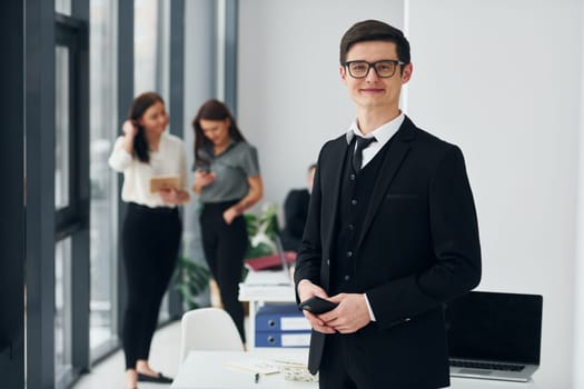 Young man with phone. Group of people in official formal clothes that is indoors in the office.