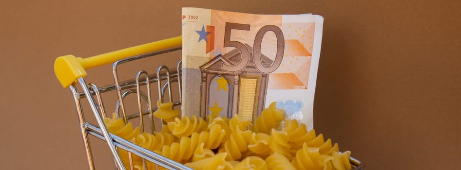 Shopping trolley cart Filled With Pasta with 50 euro paper money banknote on Beige background. Copy space for your text. Food and groceries shopping price increase, Rising food cost food crisis inflation concept. Online shopping, buy mall market shop consumer