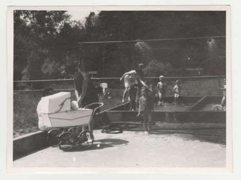 THE CZECHOSLOVAK SOCIALIST REPUBLIC - CIRCA 1970s: Vintage photo shows mothers with children at the playground - outdoor showers. Retro black and white photography. Circa 1970s.