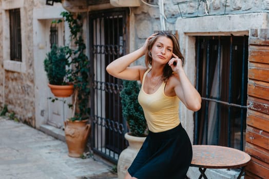 Girl tourist walking through ancient narrow street on a beautiful summer day in MEDITERRANEAN MEDIEVAL CITY , OLD TOWN bUDVA, MONTENEGRO. Young beautiful cheerful woman walking on old street at tropical town. Pretty girl looking at you and smiling