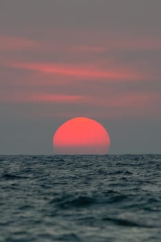 The sun fell to the sea, the bottom of the sun was blocked by the horizon. The sky is orange and the sea is dark.