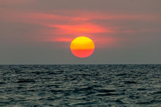 The sun is falling into the sea. , The sky is orange And the sea is dark