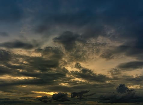 The clouds filled the sky, obscuring the light from the sun during the sunset. The sky in the middle is coloured orange from the sun. The bottom and top sky are black and dark blue from the rain clouds.