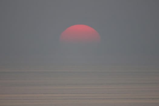 The sun is falling into the sea and being partially swallowed by the fog.  sky  is dark