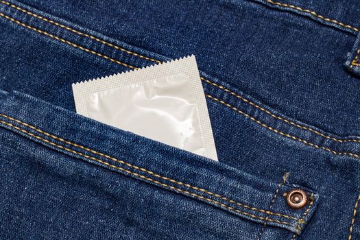 Condom in white packaging in jeans pocket close up