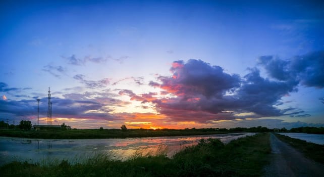 Panorama The pond reflects the light from the orange sun. The pool edge is green and yellow grass. The evening sky before the sunset is colorful.