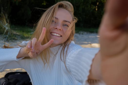 Portrait of Happy young woman take selfie on the beach sea ocean. Smiling to camera while making video call. Influencer and content creator on social media. Leisure in nature. Wellbeing unity with nature health mindfulness. Vacation and technology Enjoy outdoor lifestyle relaxation