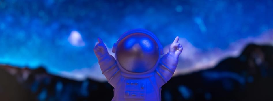 Plastic toy astronaut on universe planets background Copy space. Concept of out of earth travel, private spaceman commercial flights. Space missions and Sustainability