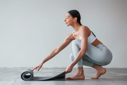 With yoga mat. Woman with sportive slim body type in underwear that is in the studio.