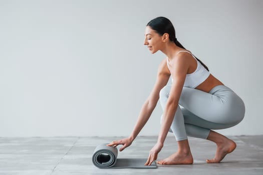 With yoga mat. Woman with sportive slim body type in underwear that is in the studio.