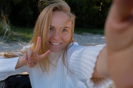 Portrait of Happy young woman take selfie on the beach sea ocean. Smiling to camera while making video call. Influencer and content creator on social media. Leisure in nature. Wellbeing unity with nature health mindfulness. Vacation and technology Enjoy outdoor lifestyle relaxation