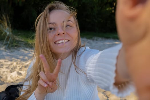 Portrait of Happy young woman take selfie on the beach sea ocean. Smiling to camera while making video call. Influencer and content creator on social media. Leisure in nature. Wellbeing unity with nature health mindfulness. Vacation and technology Enjoy outdoor lifestyle relaxation