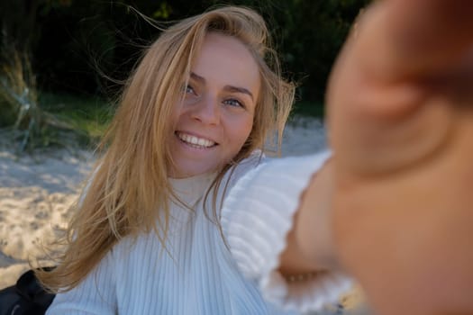 Portrait of Happy young woman take selfie on the beach sea ocean. Smiling to camera while making video call. Influencer and content creator on social media. Leisure in nature. Wellbeing unity with nature health mindfulness. Vacation and technology Enjoy outdoor lifestyle relaxation