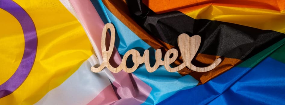 Banner Wooden word love with heart romance on Rainbow LGBTQIA flag made from silk material. Valentine's Day greeting card. Symbol of LGBTQ pride month. Equal rights. Peace and freedom. Support LGBTQIA community. Diversity equality