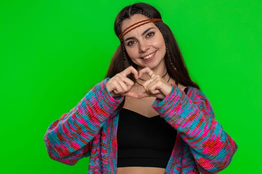 Woman in love. Smiling hippie woman 25 years old makes heart gesture demonstrates love sign expresses good feelings and sympathy. Pretty young girl isolated on chroma key background, green screen