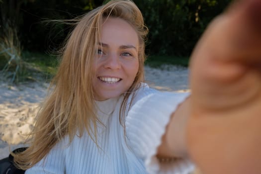 Portrait of Happy young woman take selfie on the beach sea ocean. Smiling to camera while making video call. Influencer and content creator on social media. Leisure in nature. Wellbeing unity with nature health mindfulness. Vacation and technology Enjoy outdoor lifestyle relaxation