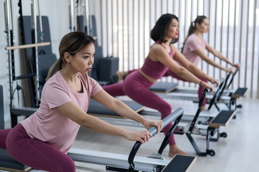 Three Asian women doing lunges on a reformer machine