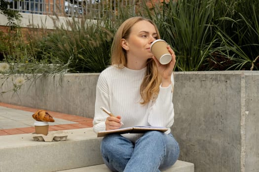 Young student study with notebook in park. Drinking coffee and eat croissants. Writing gratitude journal self reflection self discovery Outdoors warm autumn seashore.