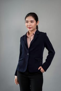 Confident young businesswoman stands on isolated background, posing in formal black suit. Office lady or manager with smart and professional appearance. Enthusiastic