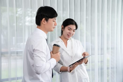 Manager advising guiding younger colleague with tablet in workplace. Couple businesspeople in formal wear working together on financial strategy as concept of teamwork and harmony in office.