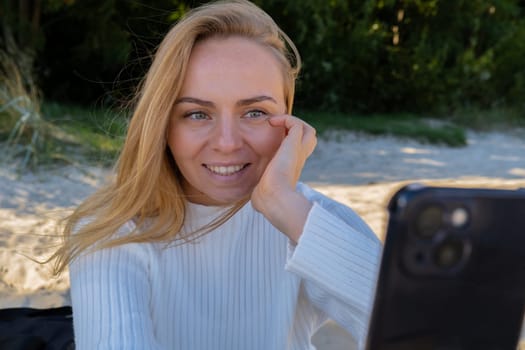 Portrait of Happy young woman take selfie on the beach sea ocean. Smiling to camera while making video call. Influencer and content creator on social media. Leisure in nature. Wellbeing unity with nature health mindfulness. Vacation and technology Enjoy outdoor lifestyle relaxation