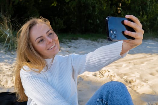 Portrait of Happy young woman take selfie on the beach sea ocean. Smiling to camera while making video call. Influencer and content creator on social media. Leisure in nature. Wellbeing unity with nature health mindfulness. Vacation and technology Enjoy outdoor lifestyle relaxation