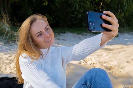 Portrait of Happy young woman take selfie on the beach sea ocean. Smiling to camera while making video call. Influencer and content creator on social media. Leisure in nature. Wellbeing unity with nature health mindfulness. Vacation and technology Enjoy outdoor lifestyle relaxation