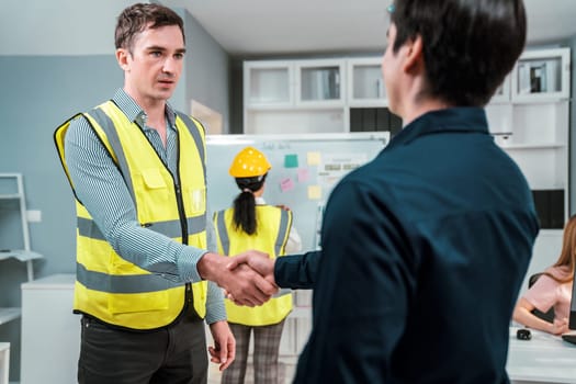 An engineer with a protective vest handshake with an investor in his office. Following a successful meeting, employee and employer form a partnership.