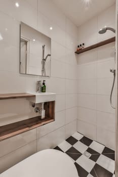 a modern bathroom with black and white tiles on the floor, sink, mirror, and shower head mounted to the wall