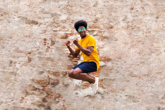 Happy young black man jumping in the air. Rustic brick and stone wall background. Happiness concept.