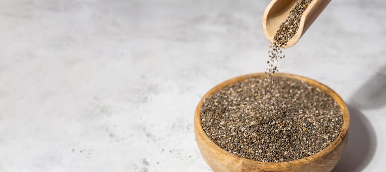 Chia seeds fall in wooden bowl. Healthy superfood rich in Omega 3 fatty acids. Dry healthy natural ingredient. Chia grains are falling. Vegetarian food