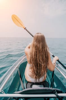 Woman in kayak back view. Happy young woman with long hair floating in transparent kayak on the crystal clear sea. Summer holiday vacation and cheerful female people having fun on the boat.