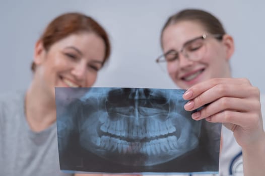 A woman doctor and a patient at the reception are discussing an x-ray of the jaw